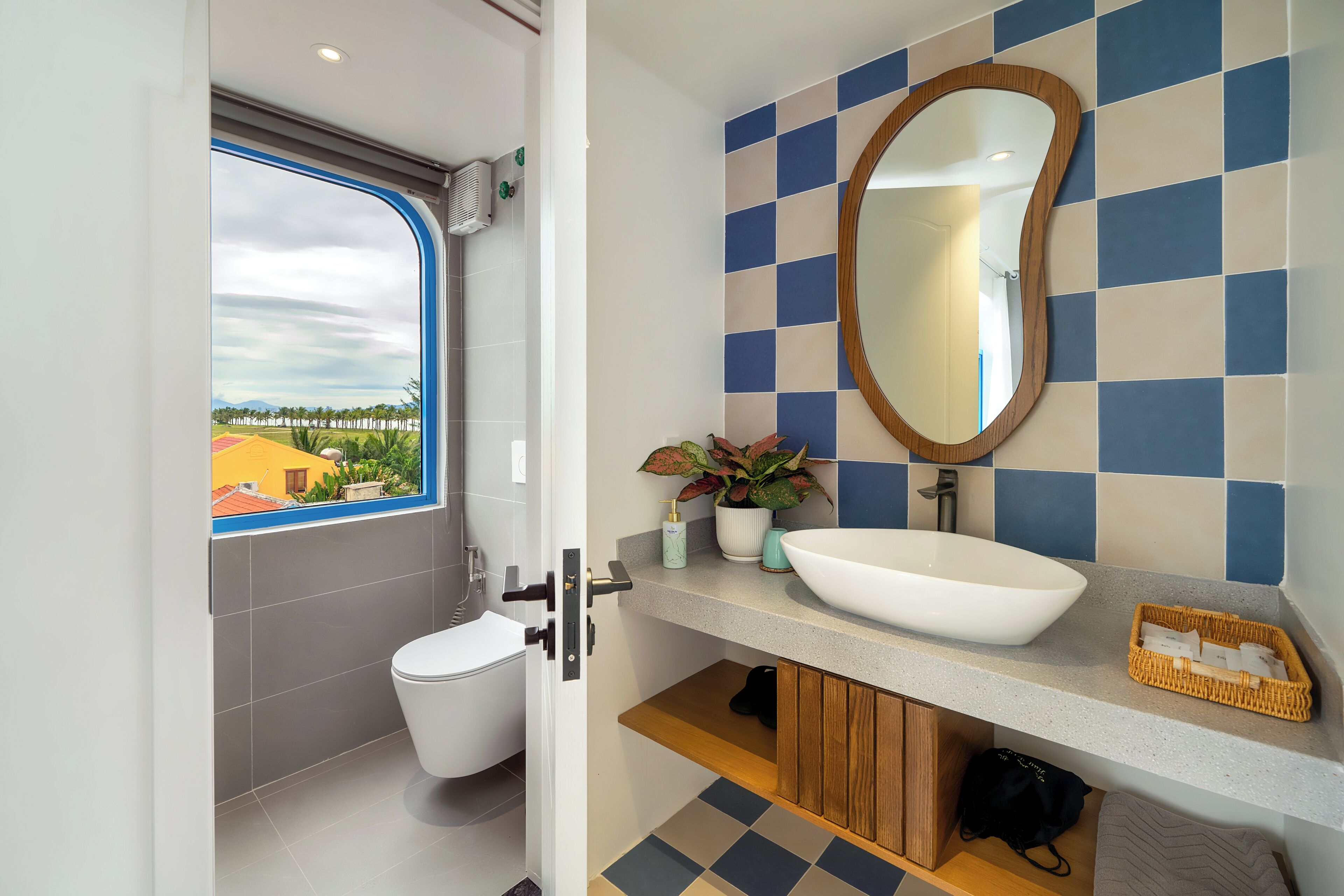A modern bathroom with a large window, a white sink, a mirror, and a potted plant.
