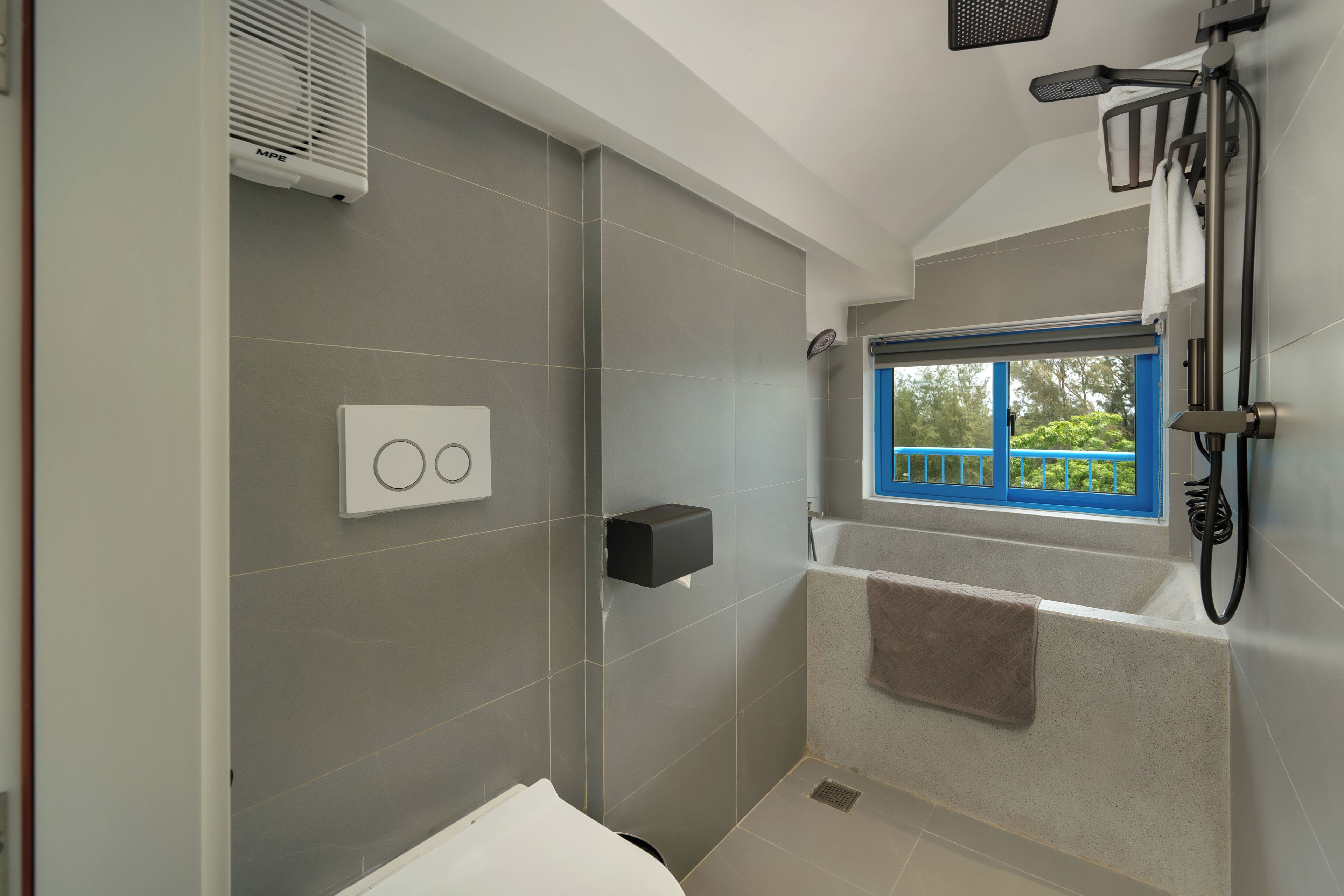 A modern bathroom with grey tiles, a built-in shower, a window with a view, and a towel rack.