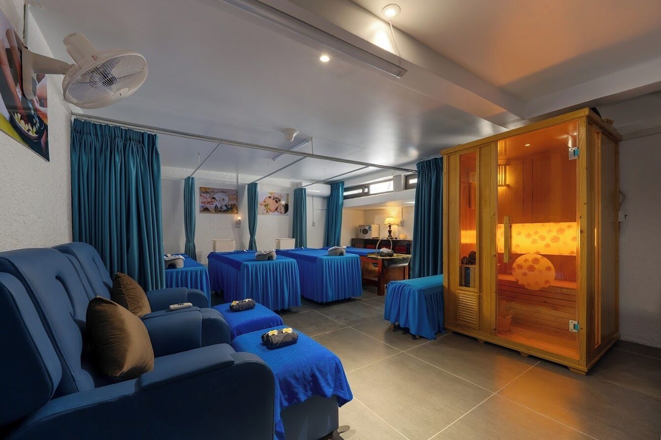 A hotel room with a sofa, two single beds, a wooden cabinet, a fan, and a window with curtains.