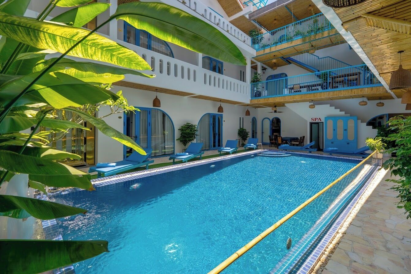 Un espace piscine avec des chaises longues, un panneau indiquant la présence d’un spa, et un immeuble à plusieurs niveaux doté de balcons.
