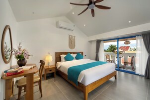 Habitación de hotel con una cama grande, un escritorio con una silla, una lámpara, un espejo y vistas al balcón exterior.