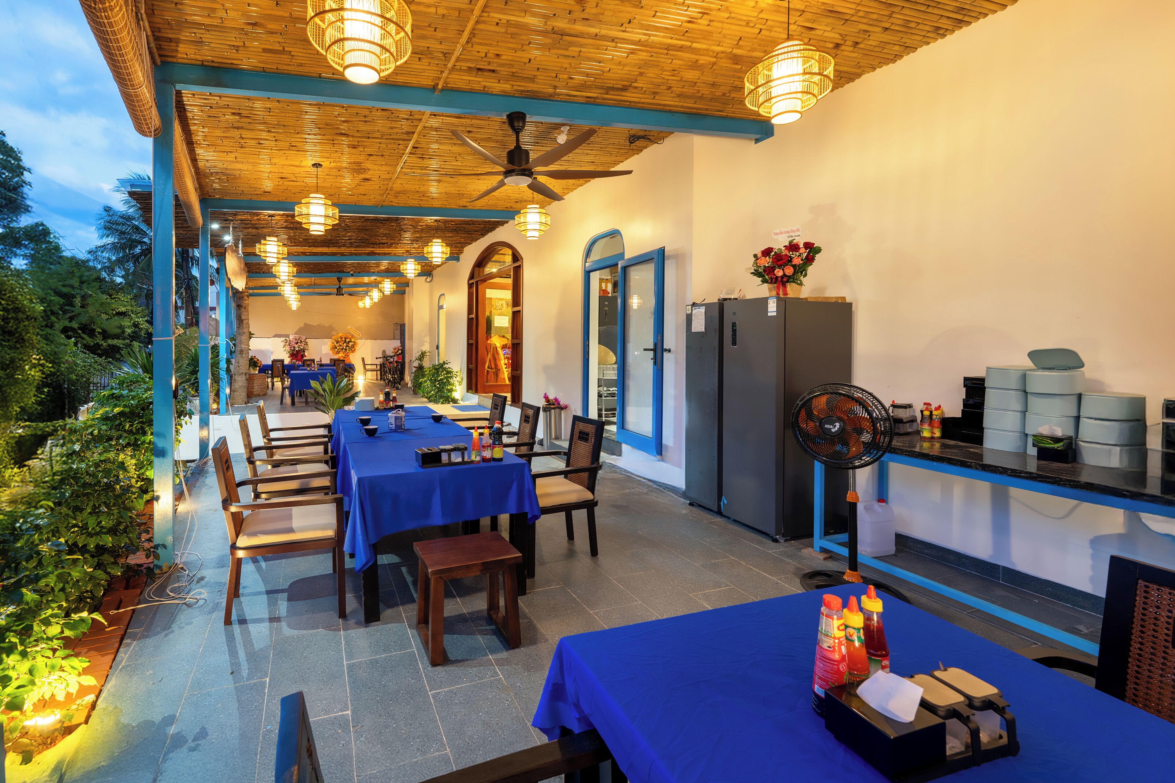 An outdoor dining area with tables and chairs, a ceiling fan, and a refrigerator.