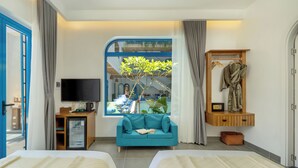 A hotel room with two beds, a TV, a small desk, a window with a view of a balcony, and a wooden cabinet with a robe. - The Linh Coastline Villa (Da Nang)