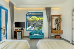 Habitación de hotel con dos camas, televisión, pequeño escritorio, ventana con vista a un balcón y armario de madera con bata.