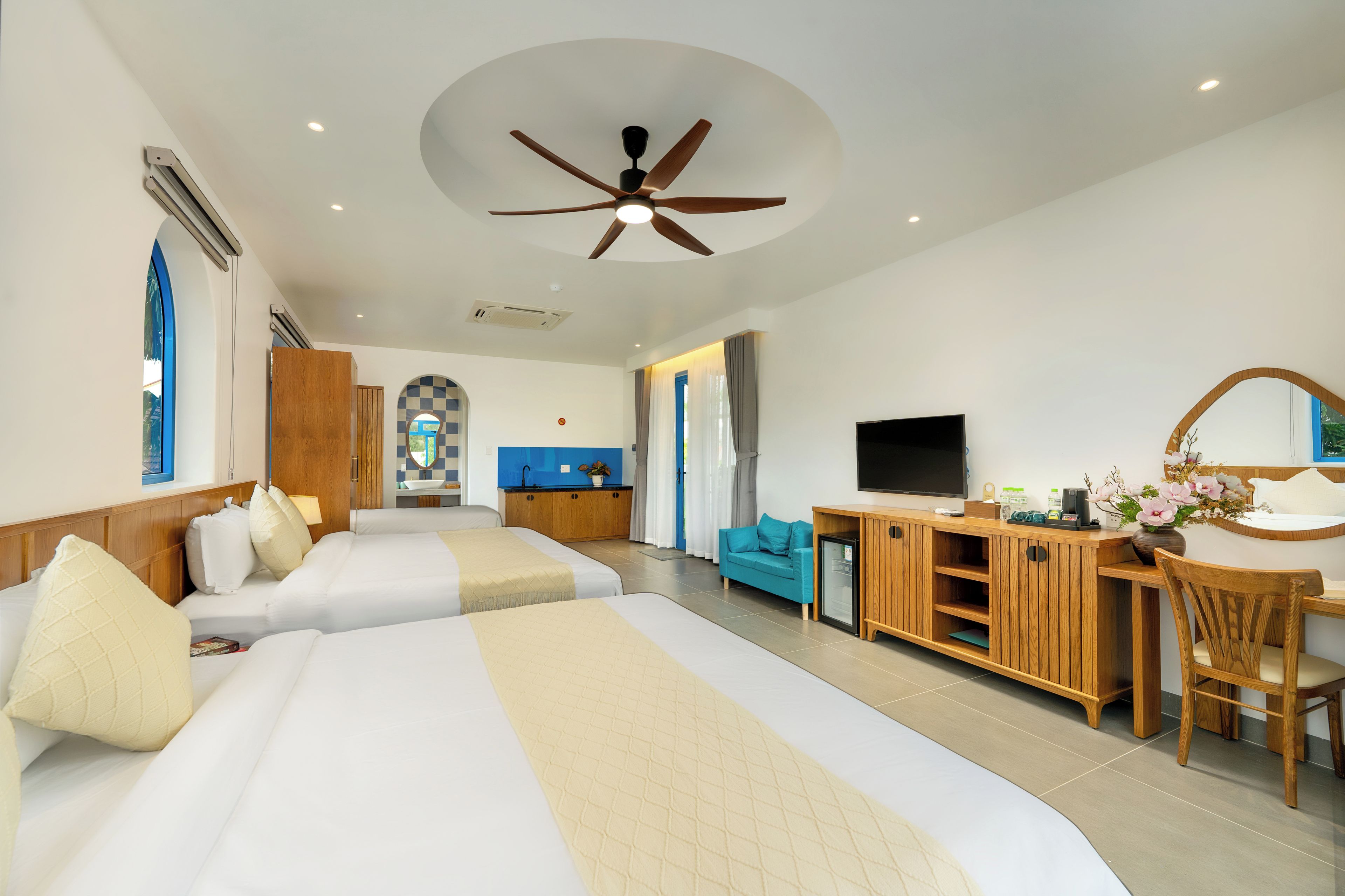 A hotel room with two beds, a desk, a television, and a ceiling fan.