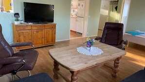 Un salon avec une table en bois, des fauteuils en cuir, un téléviseur et un réfrigérateur.