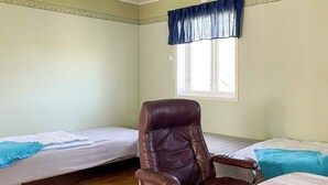 Une chambre avec deux lits simples, un fauteuil en cuir, une table en bois et une fenêtre agrémentée d’un lambrequin bleu.
