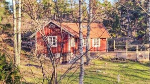 A red wooden house with a sloped roof, surrounded by trees and a grassy area. - 4 Star Holiday Home in Orno (Orno)