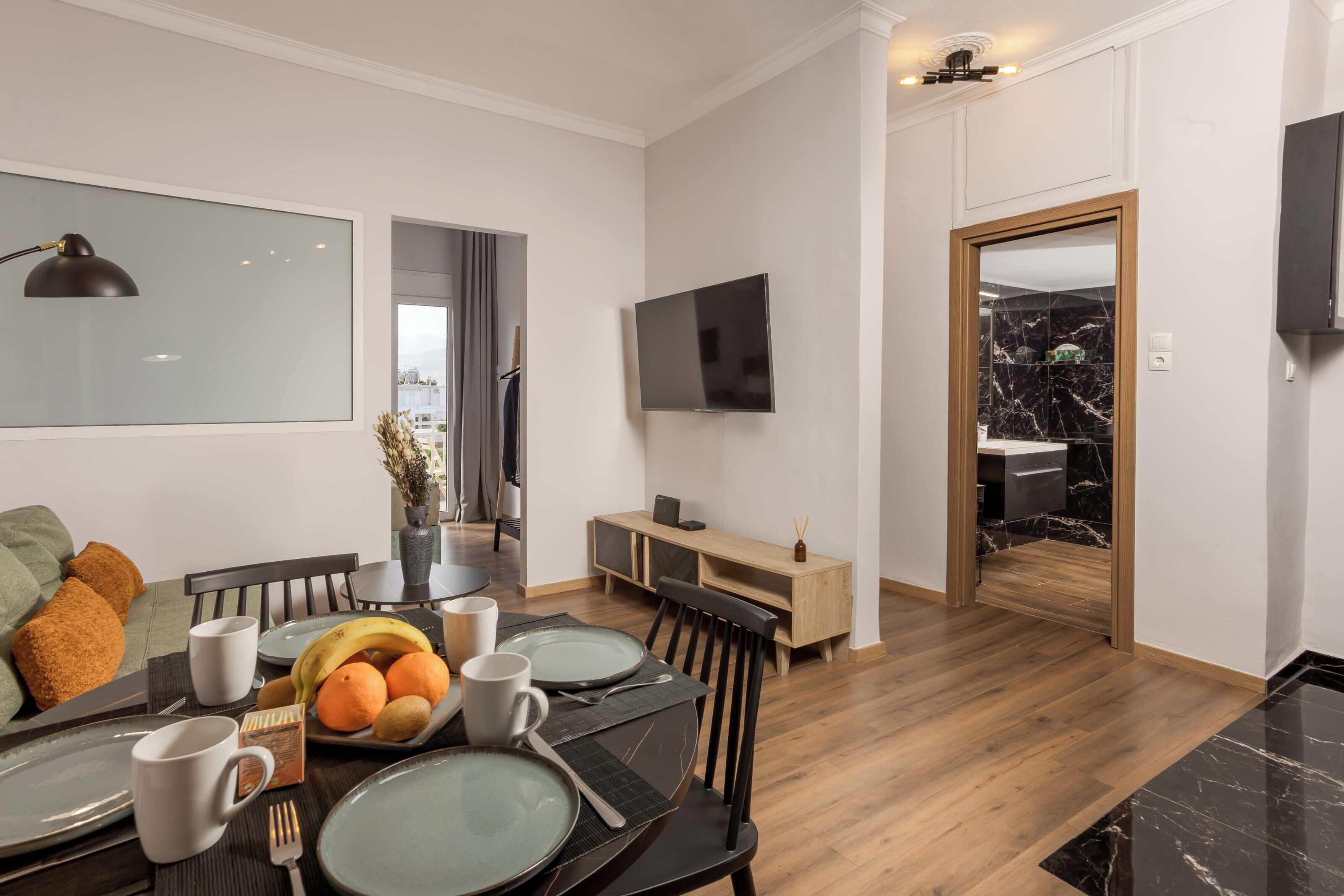 Un comedor moderno con una mesa de madera dispuesta para cuatro, un televisor montado en la pared y vistas a la cocina.