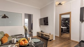 A modern dining area with a wooden table set for four, a TV mounted on the wall, and a view into the kitchen. - Zen City Apartment  (Chania)