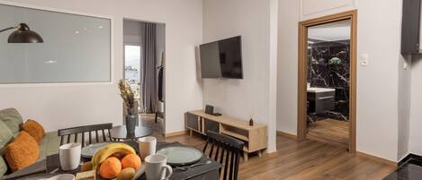 Un comedor moderno con una mesa de madera dispuesta para cuatro, un televisor montado en la pared y vistas a la cocina.