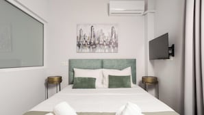 A hotel room with a bed, two bedside tables, a flat-screen TV, a painting, and an air conditioning unit. - Zen City Apartment  (Chania)