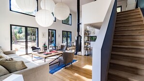 Un vaste espace de vie comprenant un grand canapé, une table basse et une bibliothèque. Un escalier mène à un niveau supérieur.