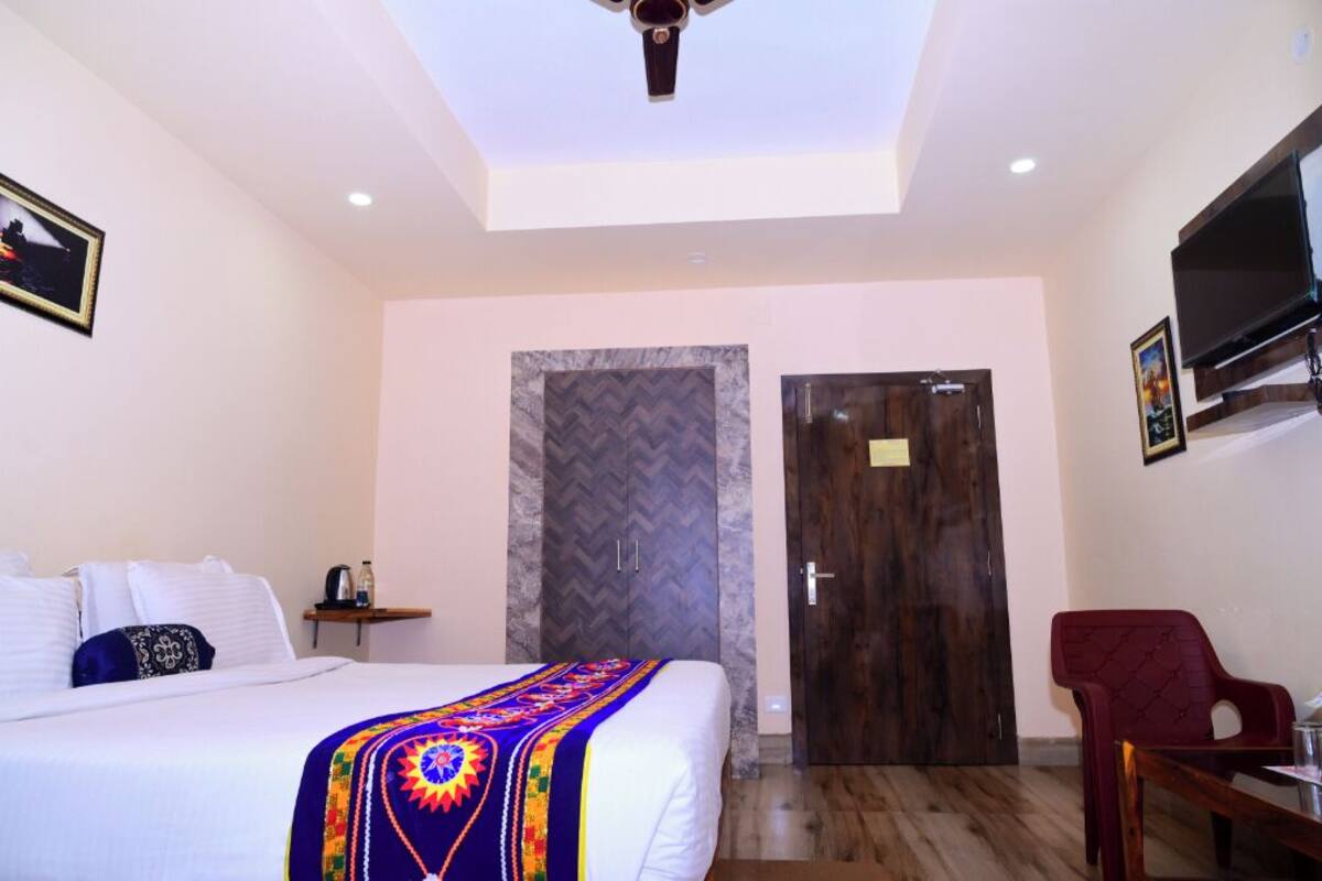 Una habitación de hotel con cama, televisor montado en la pared, puerta de madera y ventilador de techo.