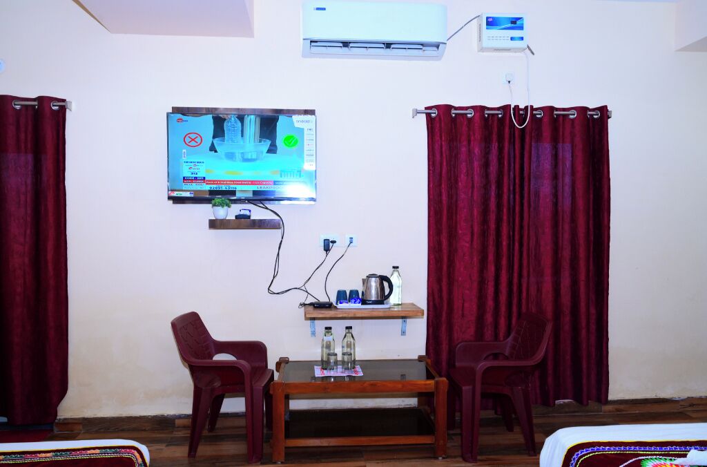 Una habitación con televisor montado en la pared, una mesa de madera con sillas, una estantería con botellas y cortinas rojas.