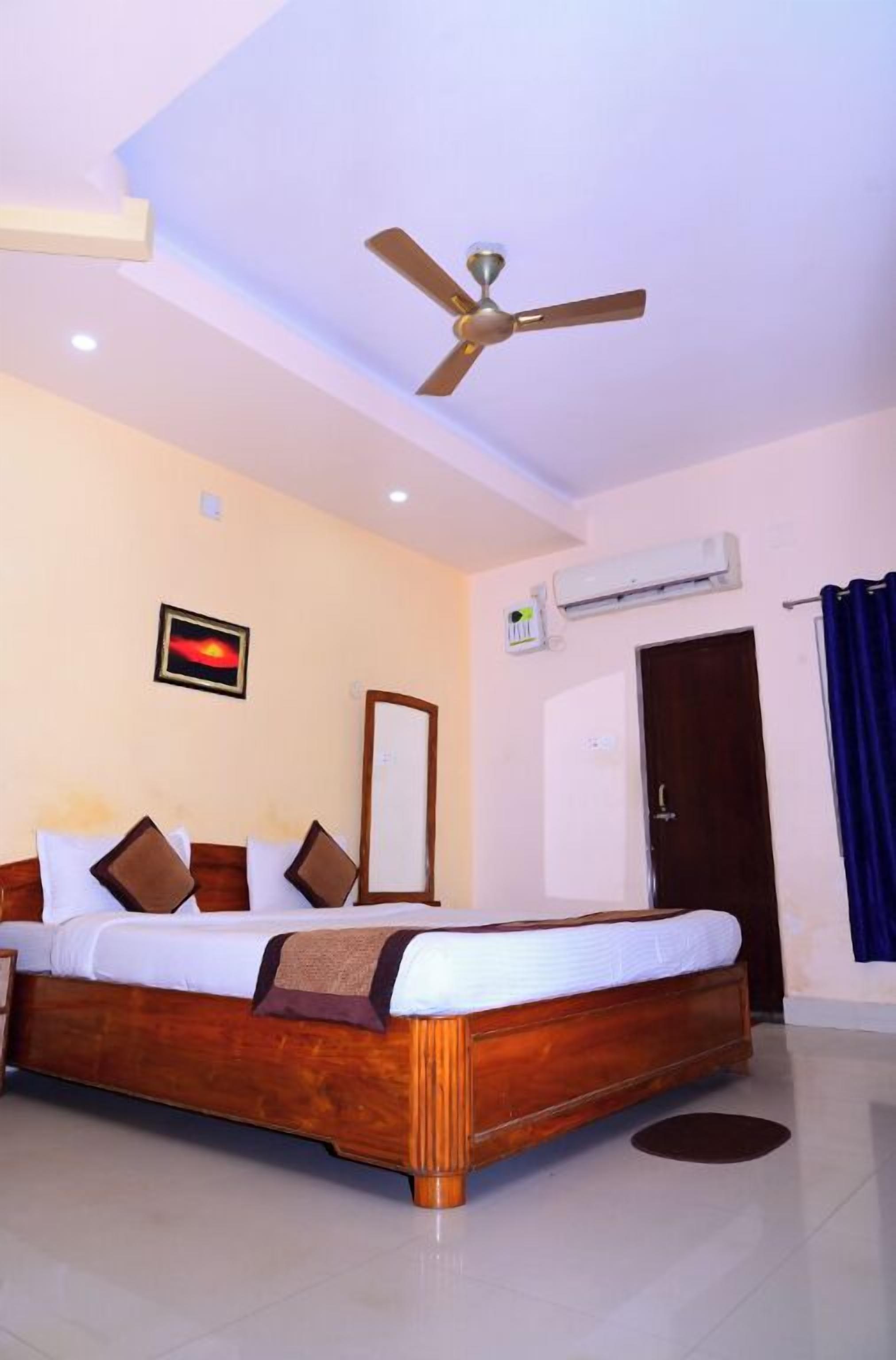 A hotel room with a wooden bed, a ceiling fan, an air conditioning unit, a door, and a framed picture on the wall.