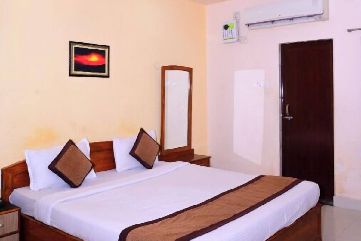 Una habitación de hotel con una cama grande, un ventilador de techo, aire acondicionado montado en la pared y un cuadro enmarcado.