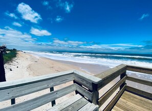 Un paseo marítimo de madera que lleva a una playa con olas rompiendo en la orilla.
