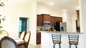 A modern kitchen with wooden cabinets, stainless steel appliances, and a central island with bar stools. - Modern 4BR House Close to Beach & All Attractions (Palm Coast)