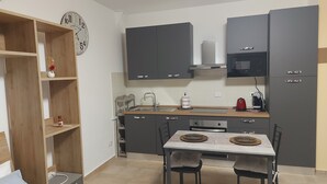 A compact kitchen with dark cabinets, a microwave, and a dining table with chairs. - Apartment in the Orti area near the University (Alessandria)