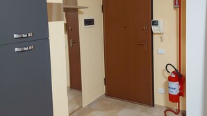 A room with a closed door, a fire extinguisher mounted on the wall, and a thermostat on the wall. - Apartment in the Orti area near the University (Alessandria)
