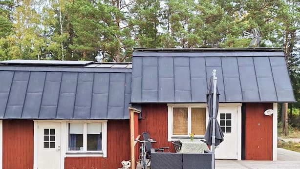 Kaksikerroksinen rakennus, jossa on tumma katto, punaiset ulkoseinät ja pieni kuisti, jossa on pöytä ja tuoleja.