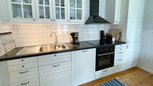 A kitchen with white cabinets, a stainless steel sink, a black stove, and a coffee maker. - 4 Star Holiday Home in Byxelkrok (Byxelkrok)