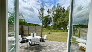 An outdoor patio with a round table and chairs, a wooden fence, and a grassy area with trees. - 4 Star Holiday Home in Byxelkrok (Byxelkrok)