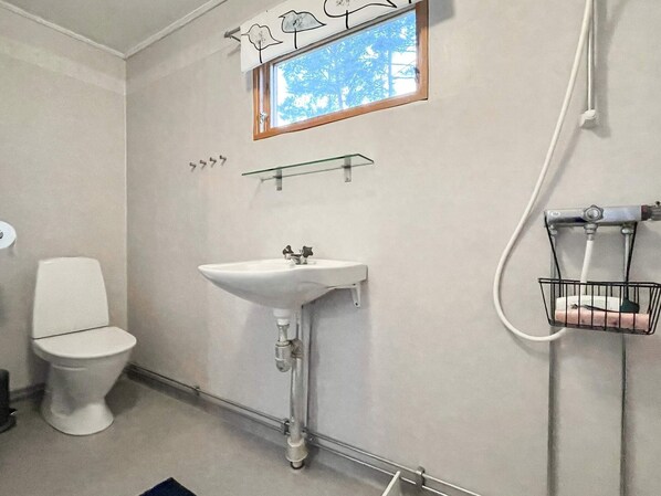 Et badeværelse med toilet, håndvask, et vindue og en bruseniche.