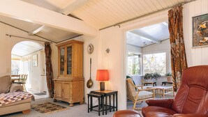 A cozy living room with a sofa, a leather armchair, a wooden cabinet, and a dining area with chairs and a table. - 8 Person Holiday Home in Jaegerspris (Jægerspris)