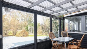 A covered patio with a table and chairs, large windows, and a view of trees and a snow-covered ground. - 8 Person Holiday Home in Jaegerspris (Jægerspris)