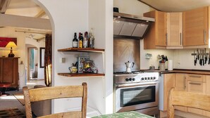 A kitchen with wooden cabinets, a stove, and a dining area with a green tablecloth. - 8 Person Holiday Home in Jaegerspris (Jægerspris)