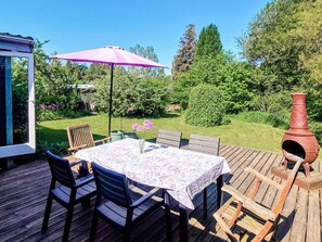 Une terrasse extérieure avec une table et des chaises, un parasol rose et un pot en terre cuite.