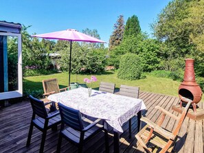 Une terrasse extérieure avec une table et des chaises, un parasol rose et un pot en terre cuite.