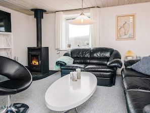 A living room with a fireplace, leather sofa, white coffee table, and a painting on the wall. - 8 Person Holiday Home in Ulfborg (Ulfborg)