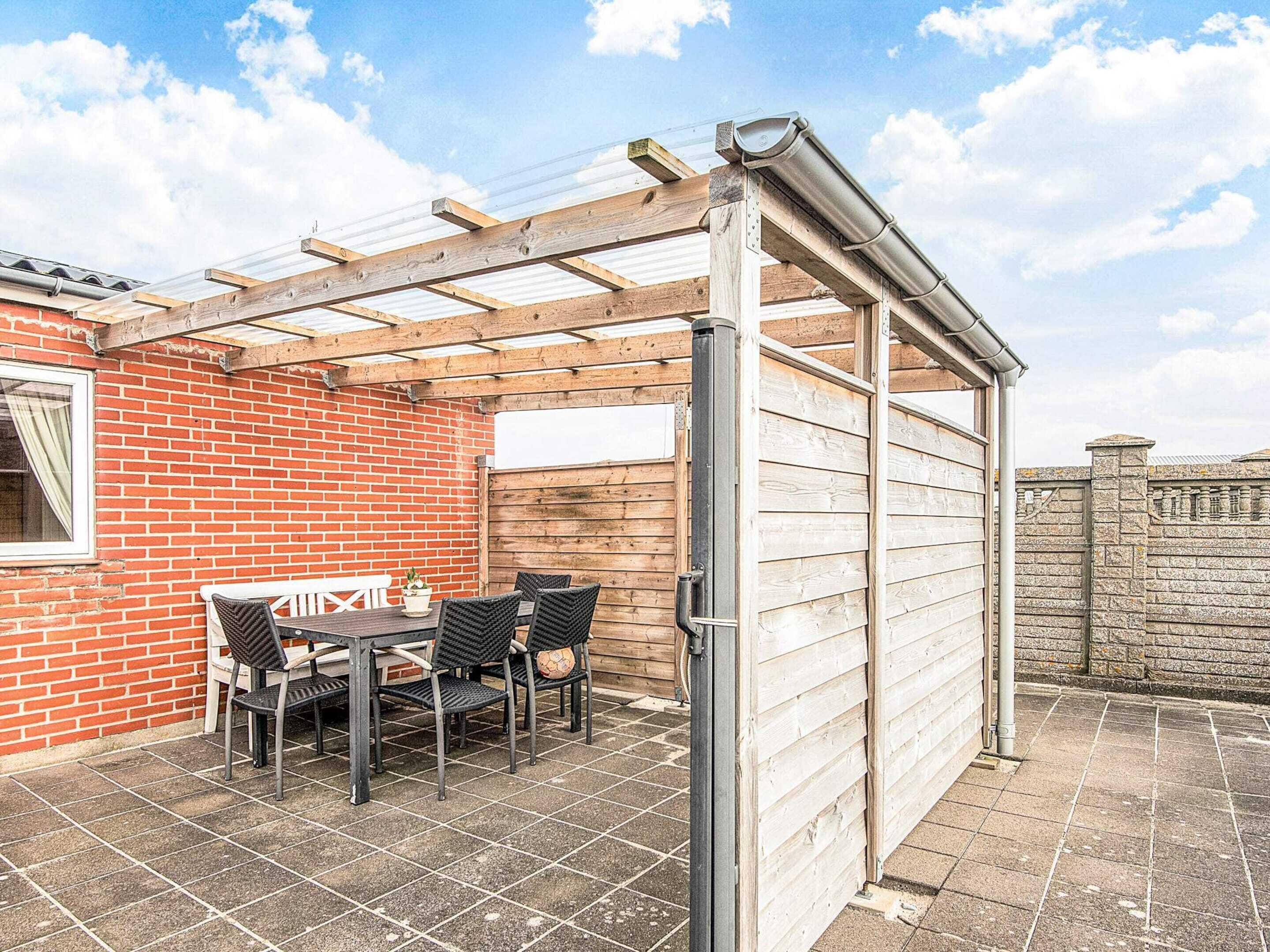 A covered patio with a table and chairs, a brick wall, and a wooden fence.