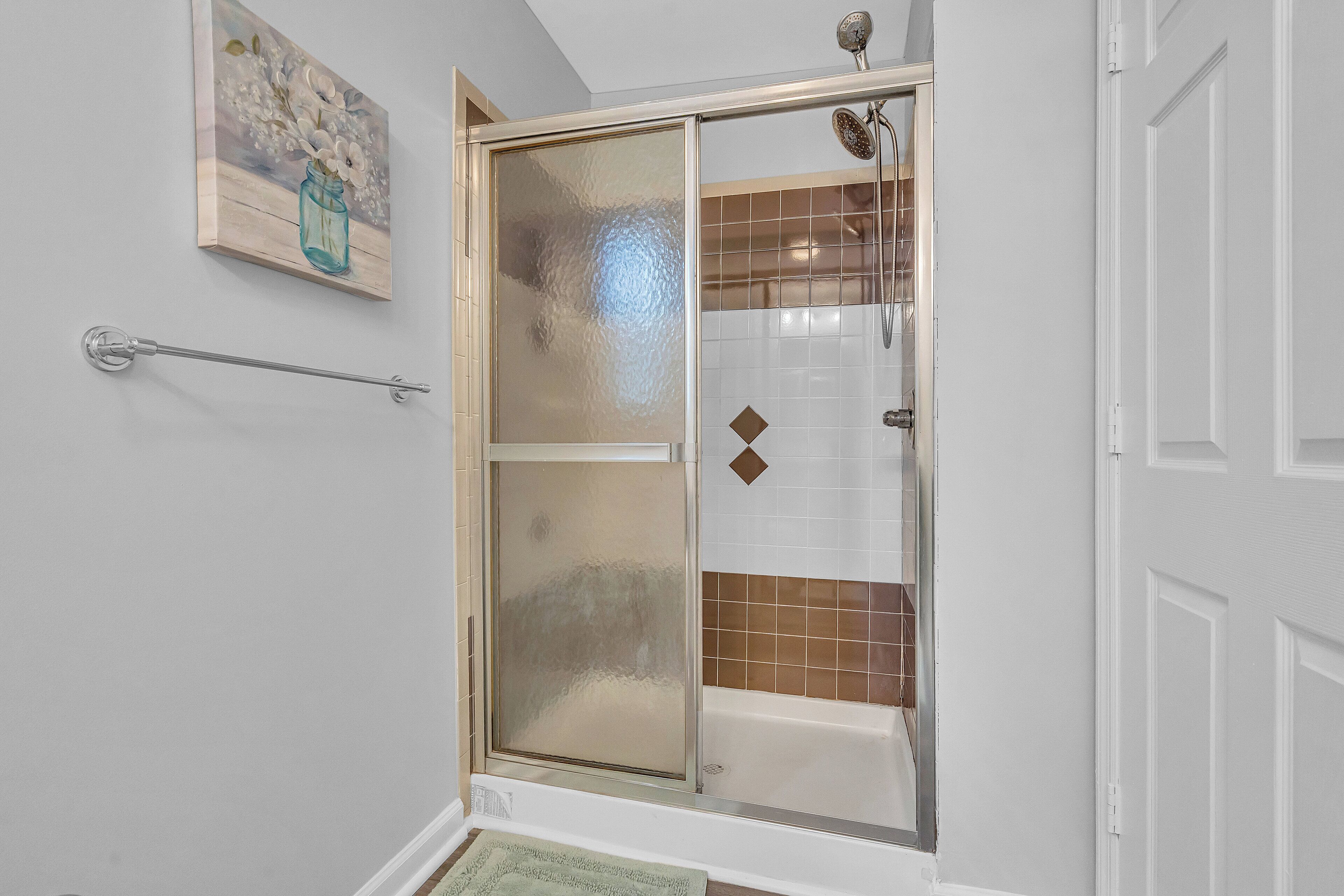 A shower area with a glass door, a towel rack, and a decorative painting on the wall.