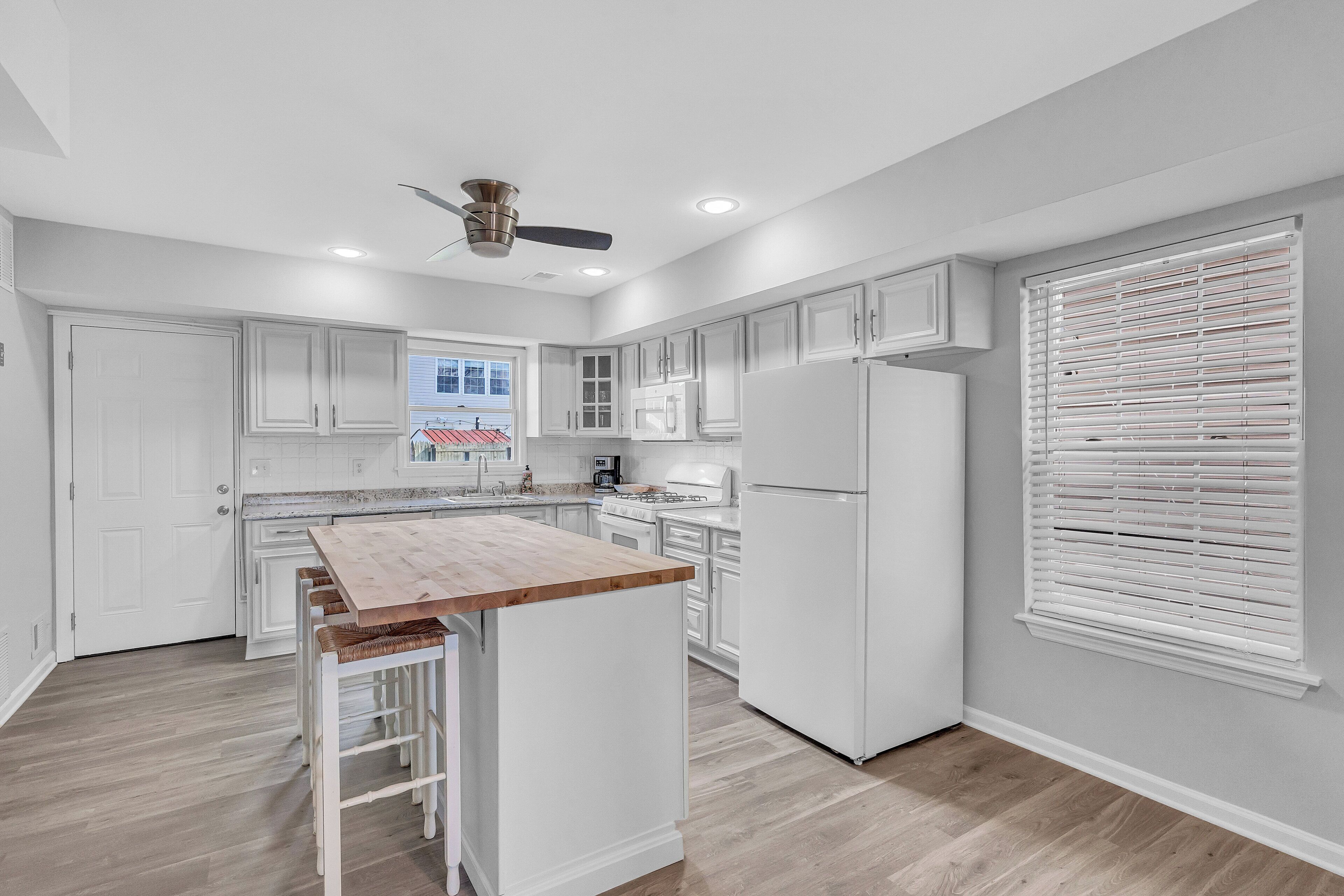 A modern kitchen with white cabinetry, a wooden island, and a ceiling fan.