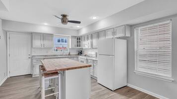 A modern kitchen with white cabinetry, a wooden island, and a ceiling fan.