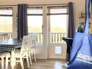 Un coin repas avec une table et des chaises, une vue à travers une porte vitrée et un sac bleu avec du texte imprimé dessus.