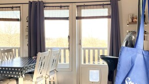 A dining area with a table and chairs, a window with curtains, and a blue bag with text. - 4 Star Holiday Home in Ljungskile (Ljungskile)
