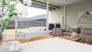 Una sala de estar moderna con un ventanal grande, una mesa de madera, un sofá color beige y un florero con flores.