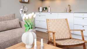 Una cocina moderna con armarios blancos, una silla de madera con respaldo trenzado y un jarrón con flores blancas sobre una mesa.