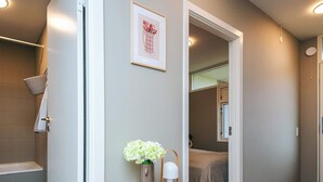 Un pasillo con una mesita de madera, un cuadro enmarcado y un espejo que refleja un dormitorio.