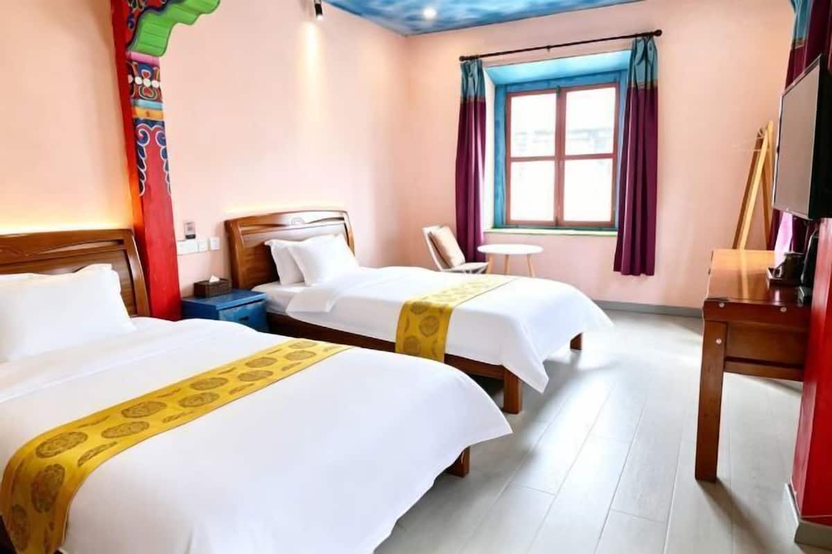 Ein Hotelzimmer mit zwei Betten, einem kleinen Tisch, einem Sessel, einem Fernseher und einem Fenster mit Vorhängen.