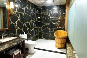 Un baño con pared de piedra, un cubo de madera, un inodoro y un lavamanos.