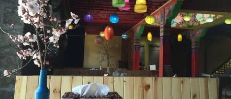 Quarto com um banco de madeira, um vaso de flores e luminárias pendentes coloridas.