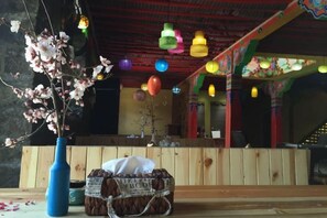 A room with a wooden bench, a vase with flowers, and colorful hanging lights. - Yading Totem Boutique Inn (Daocheng County)