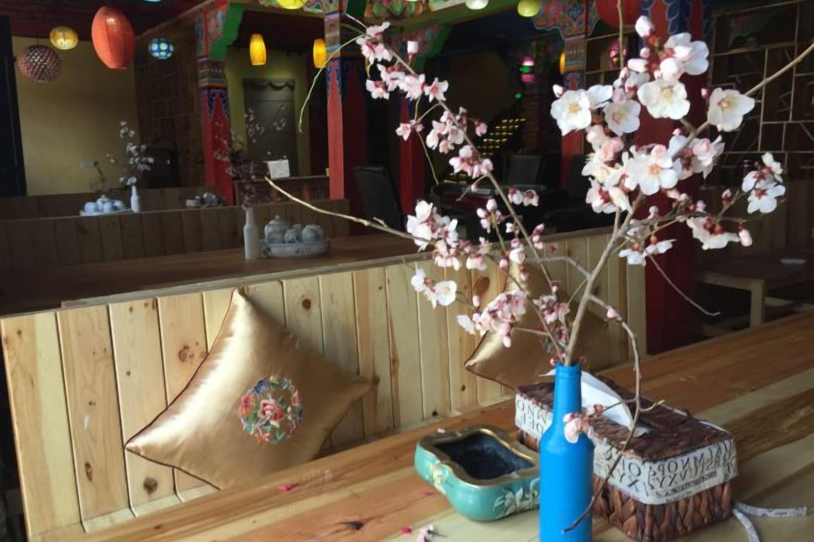 Un banco de madera con un florero de flores, un cojín decorativo y un pequeño recipiente azul.