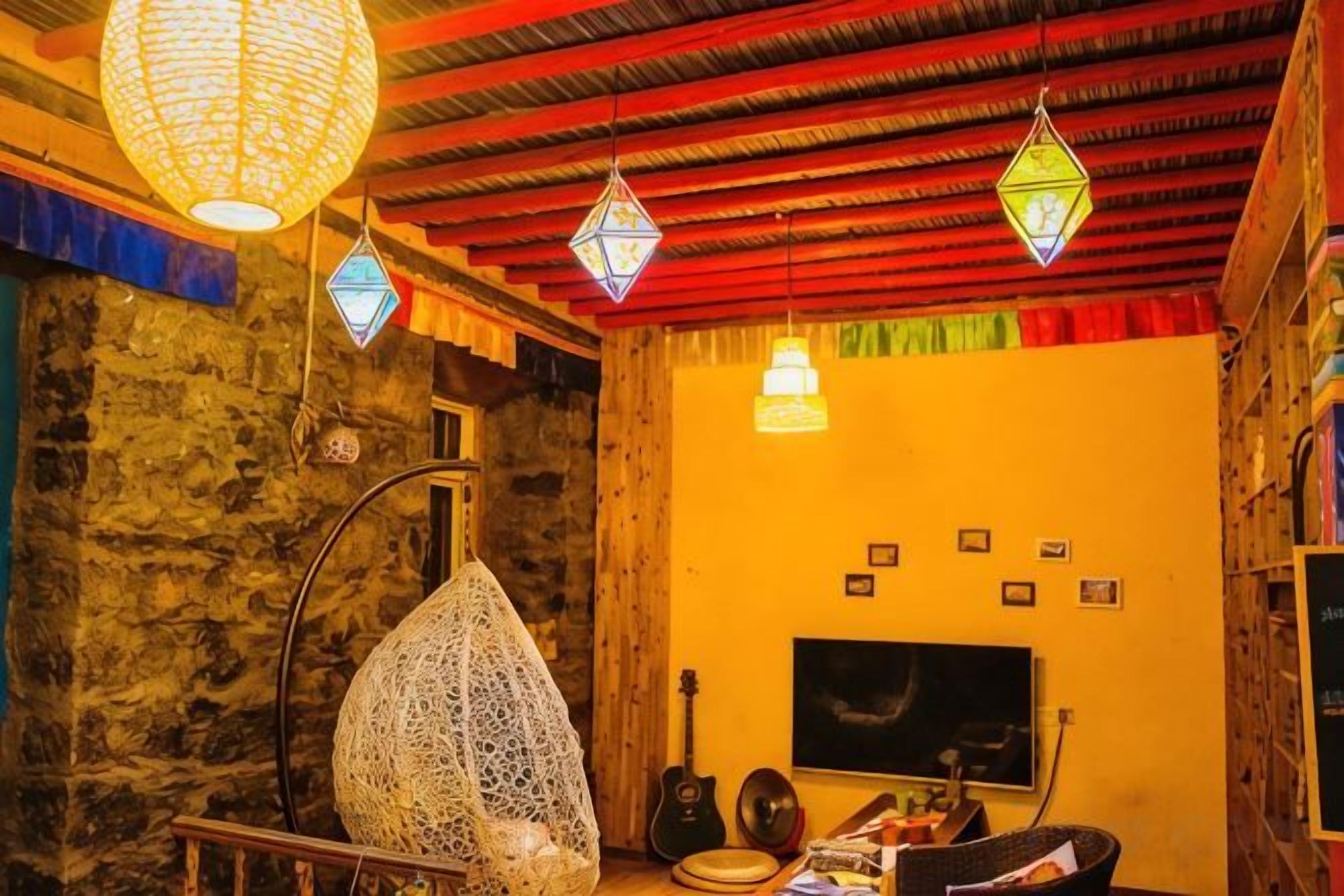 A cozy room with a stone wall, a hanging chair, a guitar, and a flat-screen TV.